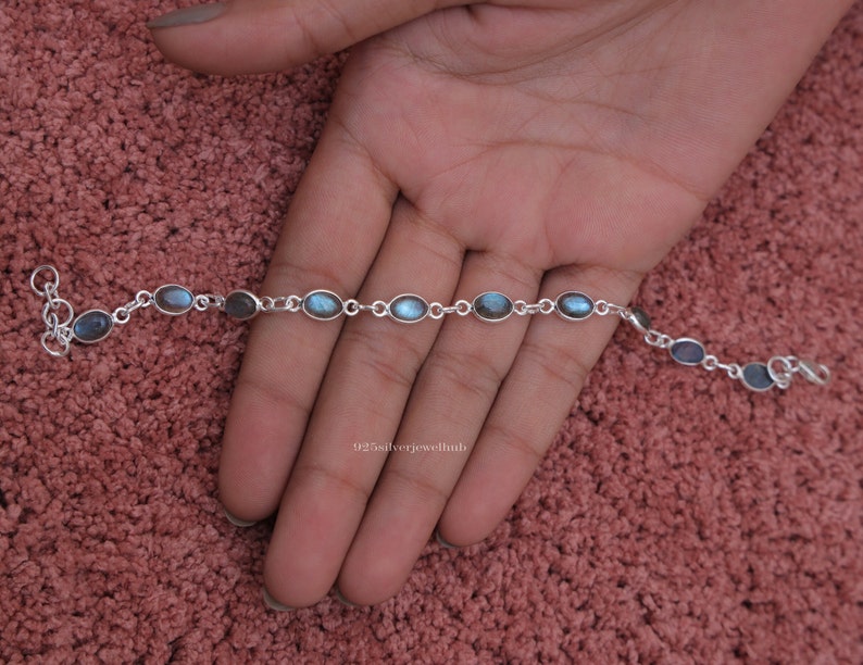 May include: A silver chain bracelet featuring a series of oval-shaped labradorite gemstones. Each stone is set in a simple silver bezel and connected by small silver circular links. The bracelet includes a lobster claw clasp and a small extender chain.