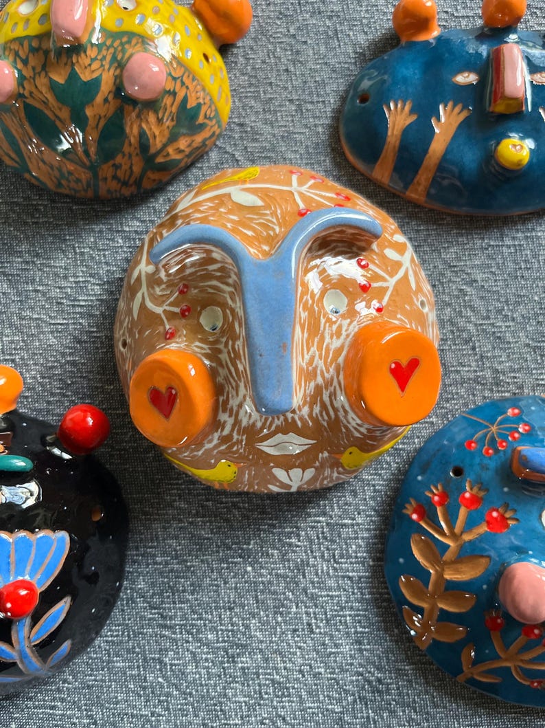May include: Five ceramic wall hangings with whimsical faces and colorful details. Each piece features unique designs and textures, including flowers, birds, and geometric patterns.