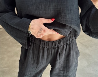 May include: A black, long-sleeved shirt and matching trousers made of a soft, textured fabric. The shirt has a relaxed fit and the trousers have an elastic waistband. The person is wearing black shoes.