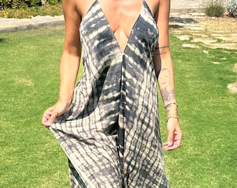 Op de afbeelding: Een maxi-jurk met tie-dye in zwart- en crèmetinten. De jurk heeft een diepe V-hals en spaghettibandjes. De stof lijkt licht en vloeiend, ideaal voor warmer weer. Het model staat op een groen gazon.