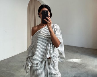 Puede incluir: Una mujer lleva una blusa blanca y negra a rayas y un pantalón a juego. La blusa es de estilo holgado y de hombros descubiertos. El pantalón es de corte holgado y de pierna ancha.