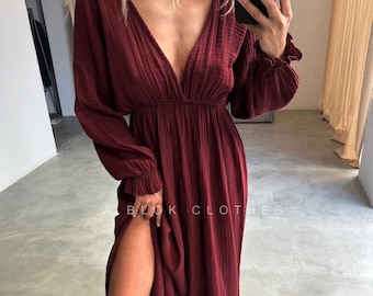 Puede incluir: Un vestido largo de color burdeos oscuro con mangas largas de tela texturizada y arrugada, escote en V profundo y cintura elástica. Las mangas tienen puños con volantes y la falda incluye una abertura lateral alta. Texto A BLOK CLOTHES.