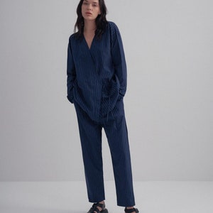 May include: A navy blue pinstripe pantsuit with a long-sleeved shirt and pants. The model is wearing black sandals.