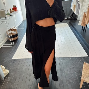 May include: A black long-sleeved crop top with a wrap skirt. The skirt has a side slit and a frayed hem.