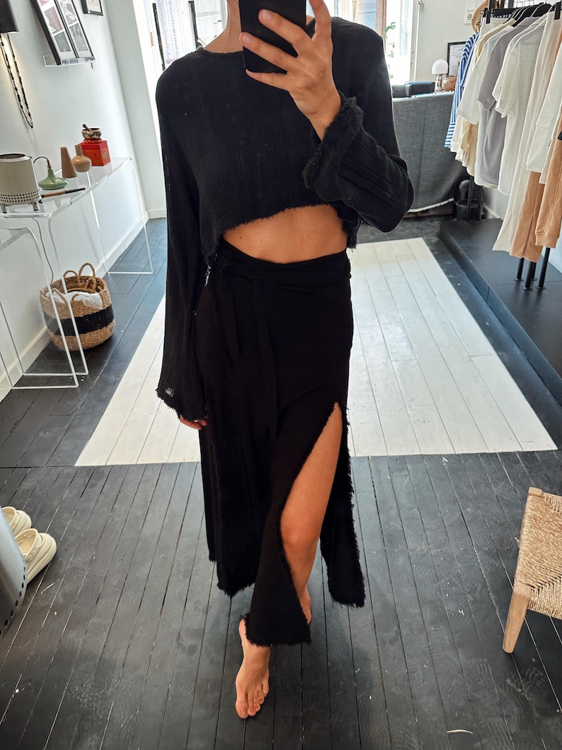 May include: A black long-sleeved crop top with a wrap skirt. The skirt has a side slit and a frayed hem.