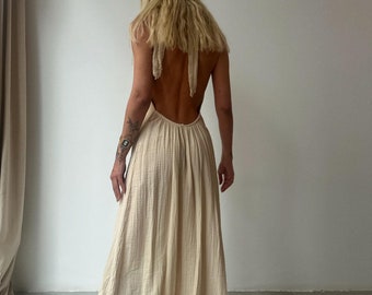 May include: A long, flowing, off-white maxi dress with a halter neckline and a tie back. The dress is made of a lightweight, gauzy fabric.