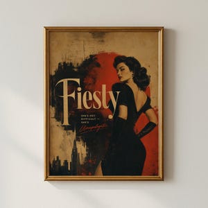 May include: A framed wall art print featuring a person in a black dress and gloves against a red and beige background. The text reads "Fiesty" and "SHE'S NOT DIFFICULT — SHE'S Unapologetic." A silhouette of a city skyline is visible at the bottom left.