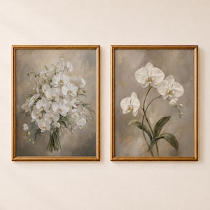 Pode incluir: Duas impressões de arte de parede retangulares em molduras douradas finas com flores de orquídea brancas. A impressão da esquerda mostra um buquê denso de orquídeas, enquanto a da direita apresenta um caule com três flores e folhas verdes.
