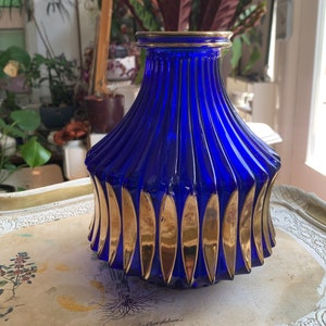 Könnte beinhalten: Eine kobaltblaue Glasvase mit goldenen Akzenten. Die Vase hat einen breiten Boden und einen schmalen Hals. Die goldenen Akzente sind in Form von Blättern und befinden sich um die Basis der Vase.