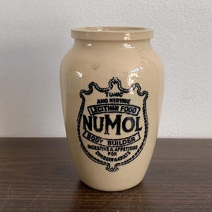 Può includere: Un barattolo di ceramica bianca con un'etichetta in bianco e nero che recita "Tonic and Nerve Lecithin Food Numol Body Builder Digestive & Appetizing for Children & Adults".