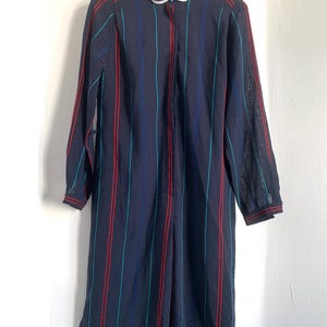 May include: A long-sleeved, navy blue dress with red and teal stripes. The dress has a white Peter Pan collar and a button-up front.