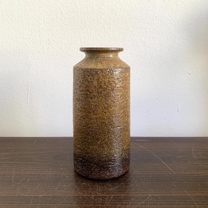Könnte beinhalten: Eine braune Keramikvase mit strukturierter Oberfläche. Die Vase hat eine leicht ausgestellte Öffnung und einen abgerundeten Boden.