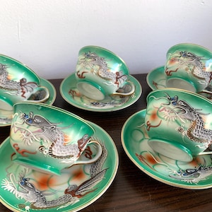 Op de afbeelding: Set van zes groene en witte theekopjes en schoteltjes met een drakenontwerp. De kopjes en schoteltjes zijn versierd met een groen en wit drakenontwerp.