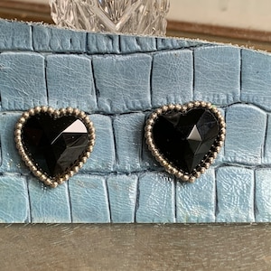 May include: A pair of black heart-shaped earrings with a silver beaded border.