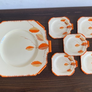 May include: A set of six square ceramic plates with an orange rim and a leaf design in shades of orange and brown.