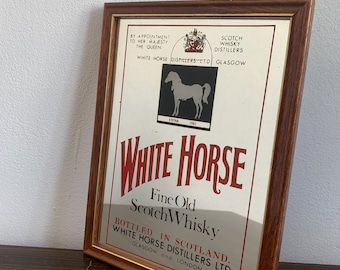 May include: A framed vintage advertisement for White Horse Fine Old Scotch Whisky. The print features a white horse silhouette on a black background, with text in red and black. The frame is a dark brown color.