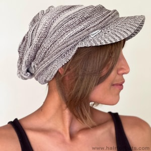 May include: A gray and white knit hat with a brim. The hat is made of a soft, textured material and has a small label on the side. The hat is designed to be worn on the head and is a stylish accessory.