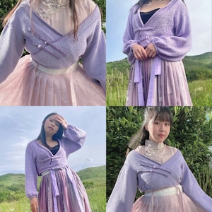 May include: A lavender knitted cardigan with a criss-cross front closure. The cardigan is worn over a light pink skirt with a floral pattern.