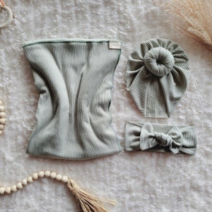 May include: A set of three sage green ribbed fabric accessories: a headband with a bow, a turban-style hat with a bun, and a long, rectangular piece of fabric.