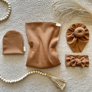 May include: A set of brown waffle knit baby accessories including a hat, headband, and a larger piece of fabric. The fabric is folded in half and has a tag that says "Lovely Little."