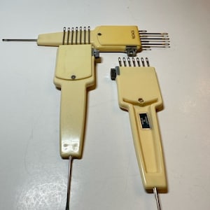 May include: Two vintage knitting tools with a cream-colored plastic body and metal needles. The tools have a label that reads "TOYO" and "MADE IN JAPAN".