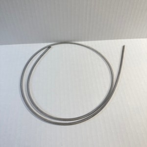 May include: A silver metal spring coil, coiled into a circle shape, on a white background.