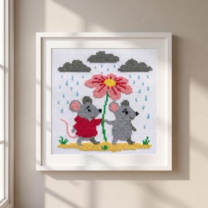 May include: A framed cross-stitch embroidery featuring two gray mice standing on a yellow patch of ground. One mouse wears a red sweater. They hold a large pink flower with a yellow center. Above them are dark gray clouds with blue rain.
