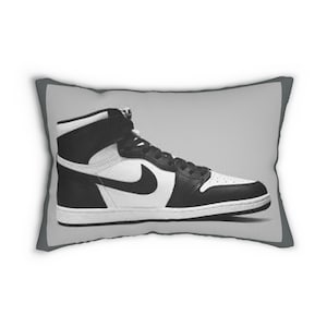 May include: A decorative pillow featuring a high-top sneaker design. The pillow showcases a black and white color scheme, with the iconic Nike swoosh prominently displayed on the side. The sneaker design is set against a gray background.