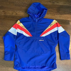 May include: A blue hooded windbreaker jacket with a white, red, and gold geometric pattern. The jacket has a zipper closure and a small Adidas logo on the front.