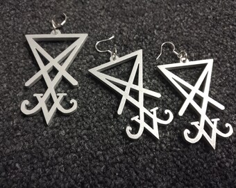 Könnte beinhalten: Drei silberne Ohrringe mit einem dreieckigen Design und einem Symbol im Inneren. Das Symbol ist ein Pentagramm mit einem Kreis in der Mitte.