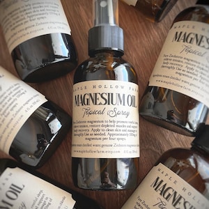 May include: Multiple dark amber glass bottles of Magnesium Oil Topical Spray are displayed on a wooden surface. The bottles feature labels with text including "Maple Hollow Farm" and product details. Each bottle contains 118 ml.