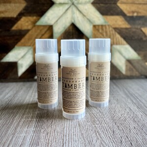 May include: Three white deodorant tubes with brown labels. The labels read "Magnesium Tallow Deodorant" and "TAMBER" with a description of the scent "cedarwood + palo santo".
