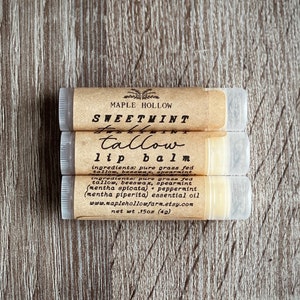 May include: Three brown tubes of Sweetmint Tallow Lip Balm with a white label. The label reads "Sweetmint Tallow Lip Balm" and lists the ingredients: pure grass fed tallow, beeswax, spearmint (mentha spicata), peppermint (mentha piperita) essential oil. The label also includes the website www.maplehollowfarm.etsy.com and the net weight of 0.15 oz (4g).