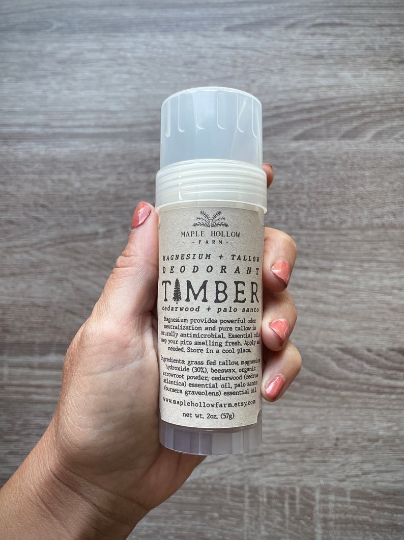 May include: A white deodorant stick with a brown label that reads "MAPLE HOLLOW FARM" and "MAGNESIUM + TALLOW DEODORANT TAMBER cedarwood + palo santo". The label also lists the ingredients and website address. The stick is 2 ounces (57g).
