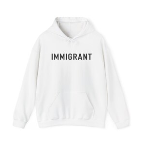 May include: White hooded sweatshirt with the word "IMMIGRANT" printed in black on the front.
