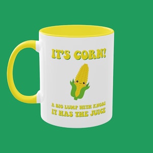Könnte beinhalten: Eine weiße Keramiktasse mit gelbem Rand und Henkel. Die Tasse zeigt ein Cartoon-Bild eines Maiskolbens mit einem lächelnden Gesicht und dem Text "It's Corn! A big lump with knobs it has the juice."