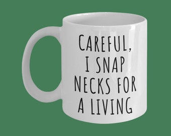 May include: White ceramic coffee mug with black text that reads "Careful, I snap necks for a living."