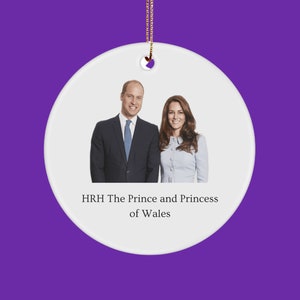 May include: A white ceramic ornament with a gold string for hanging. The ornament features a portrait of a man and woman, with the text "HRH The Prince and Princess of Wales" below the image.