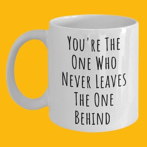 May include: White ceramic coffee mug with black text that reads "You're the one who never leaves the one behind."