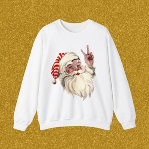 May include: White sweatshirt with a red and white striped Santa Claus graphic wearing a peace sign. The Santa Claus is smiling and has a white beard.