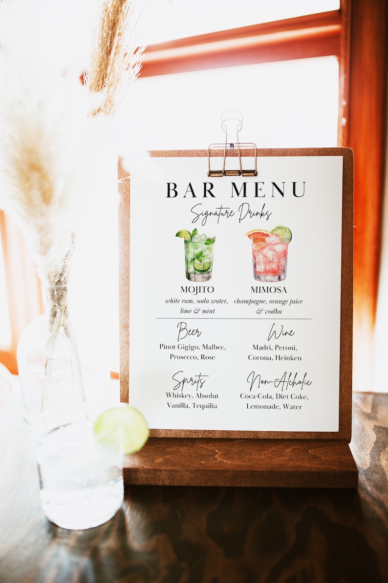 Op de afbeelding: Een wit bord met een bruin houten frame en een clip aan de bovenkant. Het bord zegt "Bar Menu" en somt signature drinks, bier, wijn, sterke drank en alcoholvrije opties op.