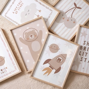 Può includere: Una collezione di stampe artistiche incorniciate con una tavolozza di colori neutri. Le stampe presentano illustrazioni fantasiose di un orso nello spazio, un razzo, ciliegie, una nuvola e un pianeta. Alcune stampe includono testo come "A SKY FULL OF STARS".