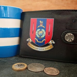 May include: A black bi-fold wallet featuring the 45 Commando Royal Marines crest, a blue and white striped mug, and three British coins. The wallet has a snap closure button with the text "KlasseK" and the crest includes the text "45 COMMANDO ROYAL MARINES".
