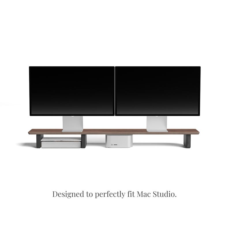 K&ouml;nnte beinhalten: Ein Holzst&auml;nder mit zwei Ablagen, der f&uuml;r zwei Computermonitore und einen Mac Studio-Computer ausgelegt ist. Der St&auml;nder ist aus dunklem Holz gefertigt und hat ein modernes Design.