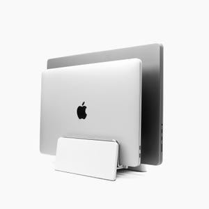 Op de afbeelding: Een witte laptopstandaard met een zilveren laptop erop. De laptop is gesloten en heeft een Apple-logo op de achterkant.