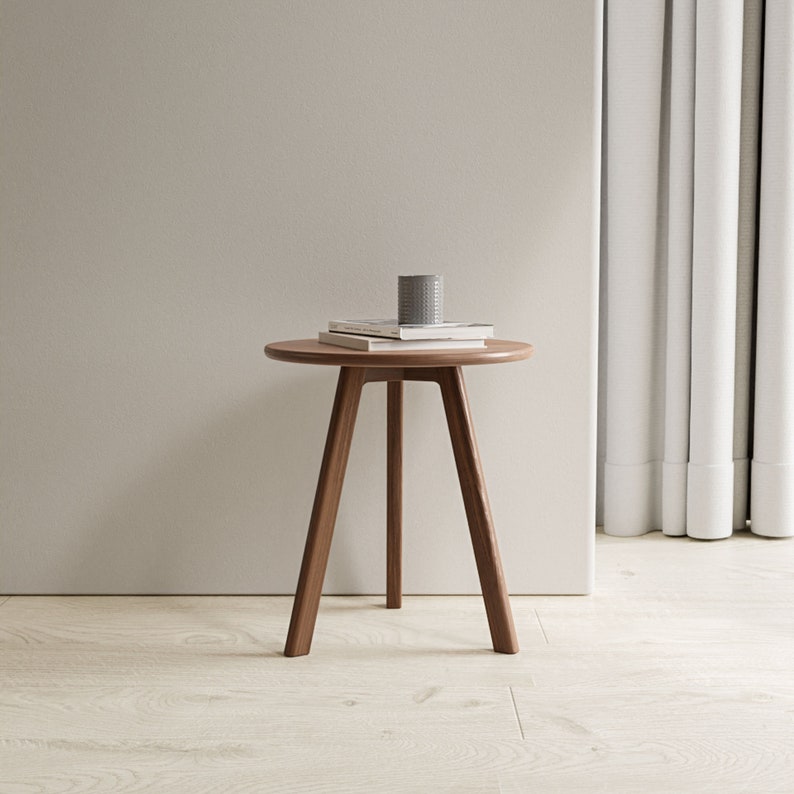 May include: A round wooden side table with three legs. The table is made of walnut wood and has a natural finish. The table is 20 inches in diameter and 18 inches tall.