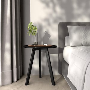 Puede incluir: Una mesa auxiliar negra con una tapa redonda de madera y tres patas. Un peque&ntilde;o jarr&oacute;n con hojas verdes se encuentra sobre la mesa.