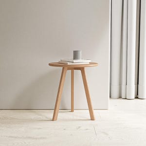 May include: A light wood round side table with three legs. The table has a simple design and is perfect for a small space.