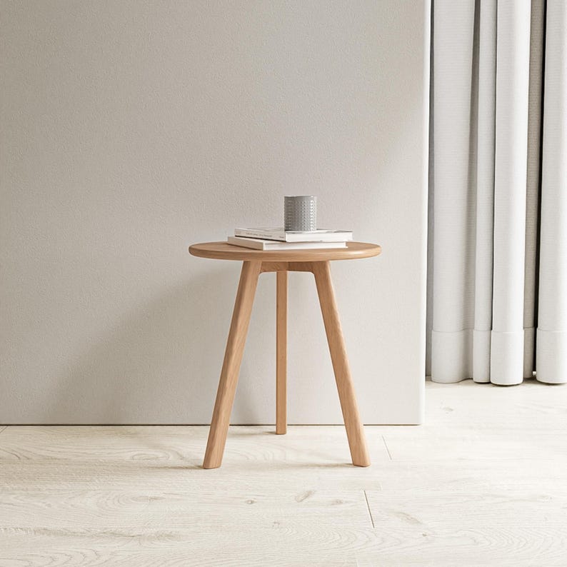 May include: A light wood round side table with three legs. The table has a simple design and is perfect for a small space.