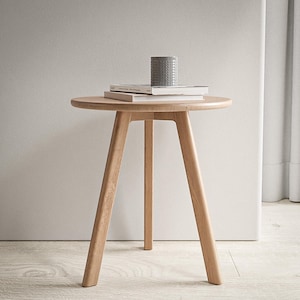 Puede incluir: Una mesa auxiliar redonda de madera clara con tres patas. La mesa tiene un acabado de madera natural y est&aacute; hecha de madera maciza. La mesa tiene un di&aacute;metro de 61 cm y una altura de 51 cm.